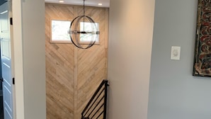 Ein Korridor mit Holzboden, einer Wand mit Fischgrätmuster, einem schwarzen Geländer und einer Pendelleuchte.