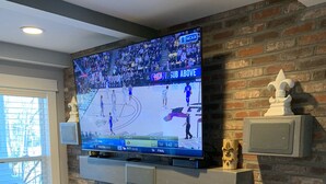 Ein Wohnzimmer mit einem Flachbildfernseher an einer Ziegelwand, einem Kamin darunter und einem Fenster links.