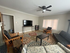 A living room with a ceiling fan, a flat-screen TV on a wooden stand, a patterned rug, and a gray sofa.