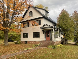 A two-story house with a brick foundation, a red door, and a small front porch. - Large Historic home near Swedetown Trails-pet friendly (Calumet)