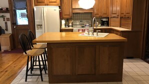 A kitchen with wooden cabinets, a central island with a sink, and a hanging light fixture. - Luxury listing close to stadium and downtown (State College)