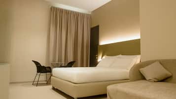 A modern hotel room with a large bed, a sofa, a small table, and a chair.