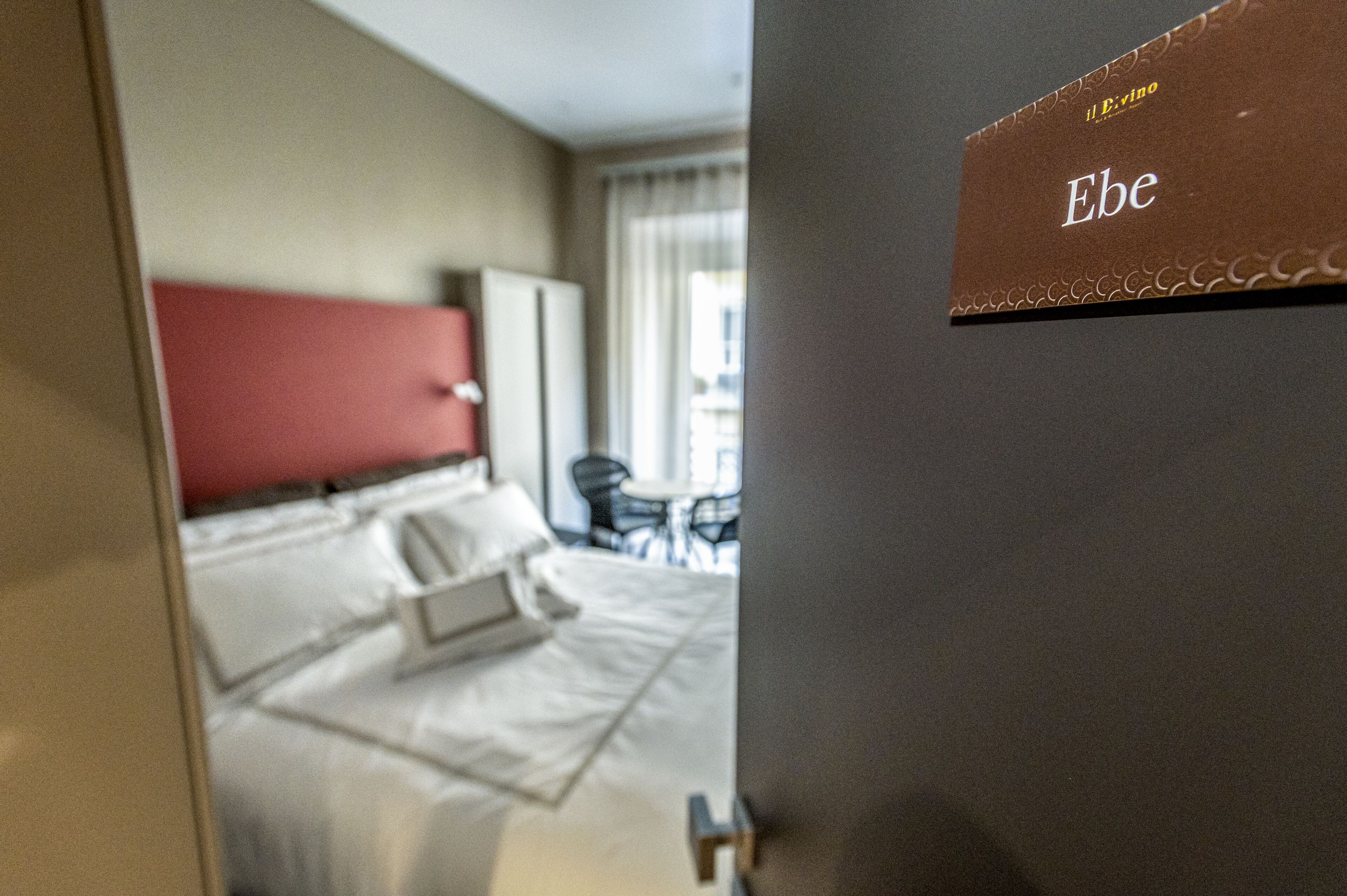 A hotel room with a bed, a desk, and a chair. There is a sign on the wall that reads "Ebe".
