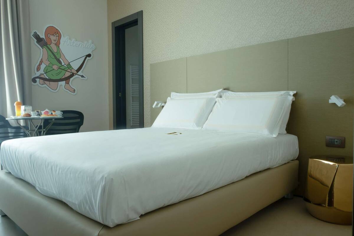 Habitación de hotel con una cama grande, una mesita con alimentos para el desayuno, una silla y un adorno en la pared.