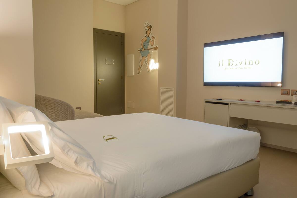 Habitación de hotel con cama, escritorio y televisor que muestra 'il Divino Bed & Breakfast Napoli'.