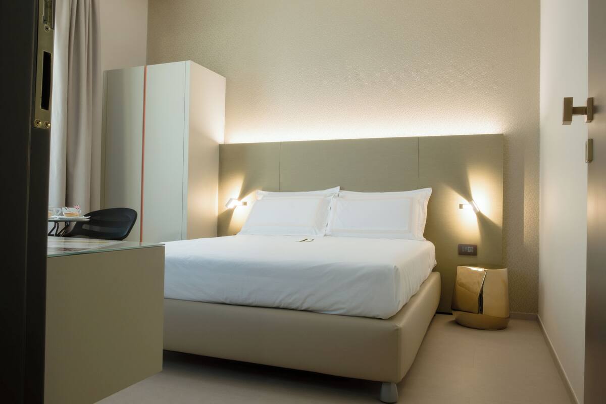 Una habitación de hotel con cama, mesita de noche, silla y una pequeña mesa con lámpara.
