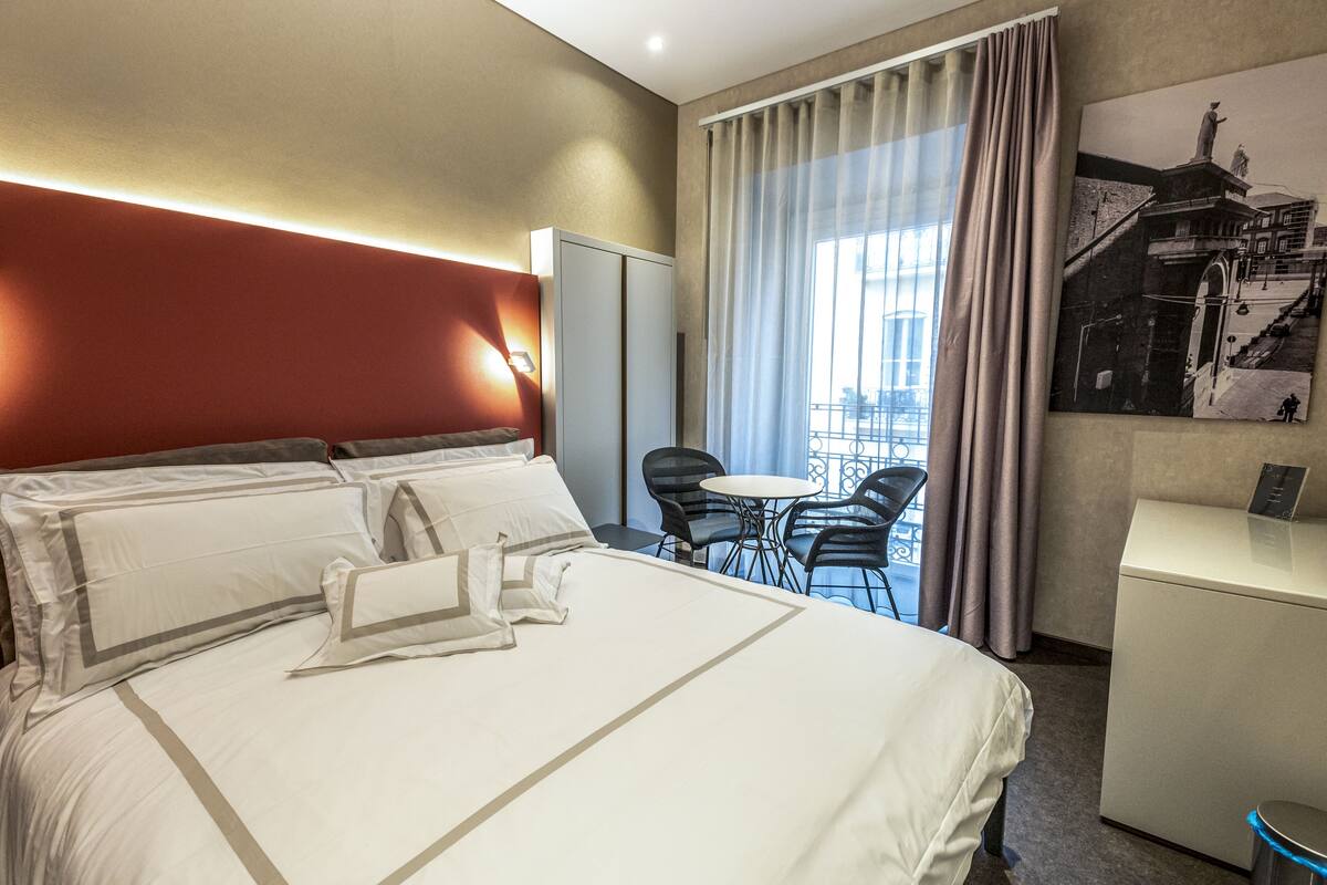Una habitación de hotel con una cama grande, un escritorio, una silla y vistas a la ciudad por la ventana.