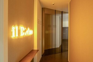 A hallway with a neon sign reading "il Drino" and a wooden bench.
