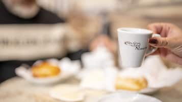 Une main tenant une tasse blanche avec du texte, une assiette avec une pâtisserie et une cuillère sur une table.
