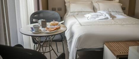 A hotel room with a bed, a table with breakfast items, and a chair.