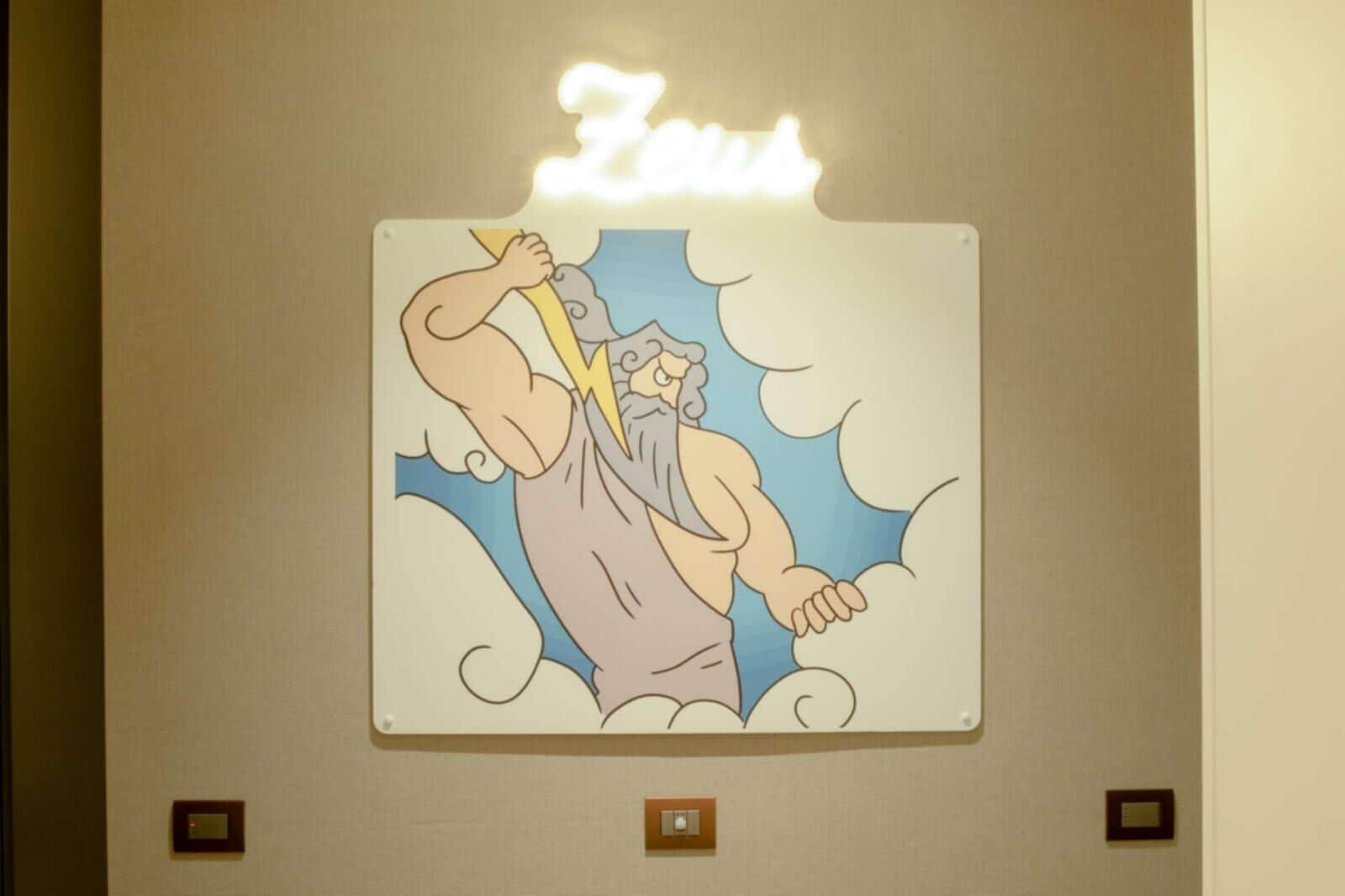 Une enseigne murale représentant un personnage de dessin animé tenant un éclair, avec le mot « Zeus » écrit au-dessus.