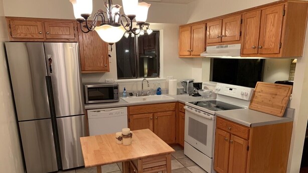 A compact kitchen with wooden cabinets, a stainless steel refrigerator, a microwave, an oven, and a sink. - You're going to love it here! (Virginia Beach)
