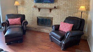 A living room with two leather armchairs, a fireplace, and a mounted TV. - You're going to love it here! (Virginia Beach)