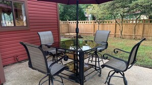 A patio with a table and four chairs, a glass-top table, and a wooden fence in the background. - You're going to love it here! (Virginia Beach)
