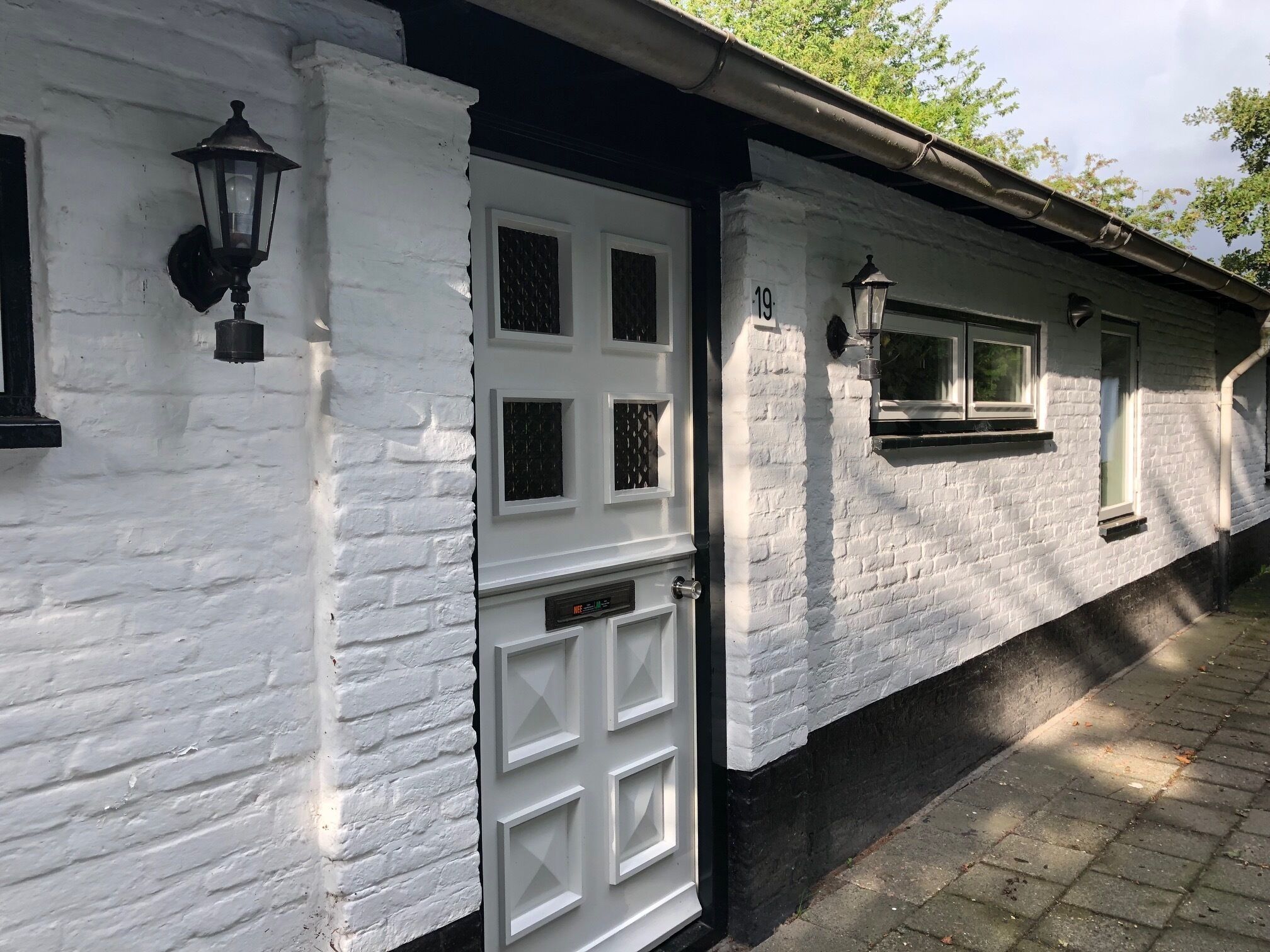 A white brick building with a white door, two windows, and a black lantern on the wall.