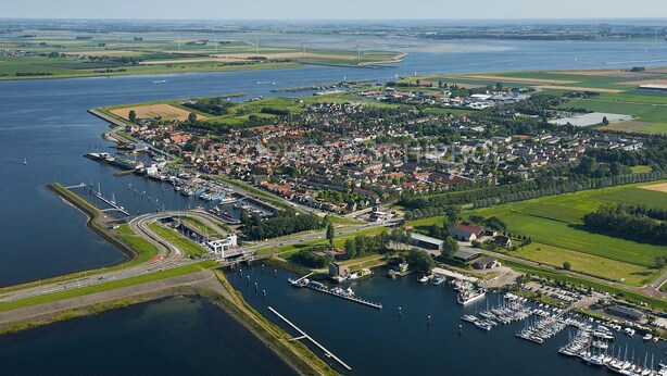 Vista aérea de un pueblo costero con un puerto deportivo, zonas residenciales y campos verdes.