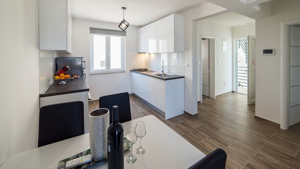 A modern kitchen with white cabinets, a dining area with a table, and a small island with a sink. - Villa Maja (Konavle)