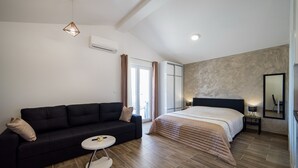 A modern hotel room with a black sofa, a round coffee table, a large bed with a beige quilt, and a wooden floor. - Villa Maja (Konavle)