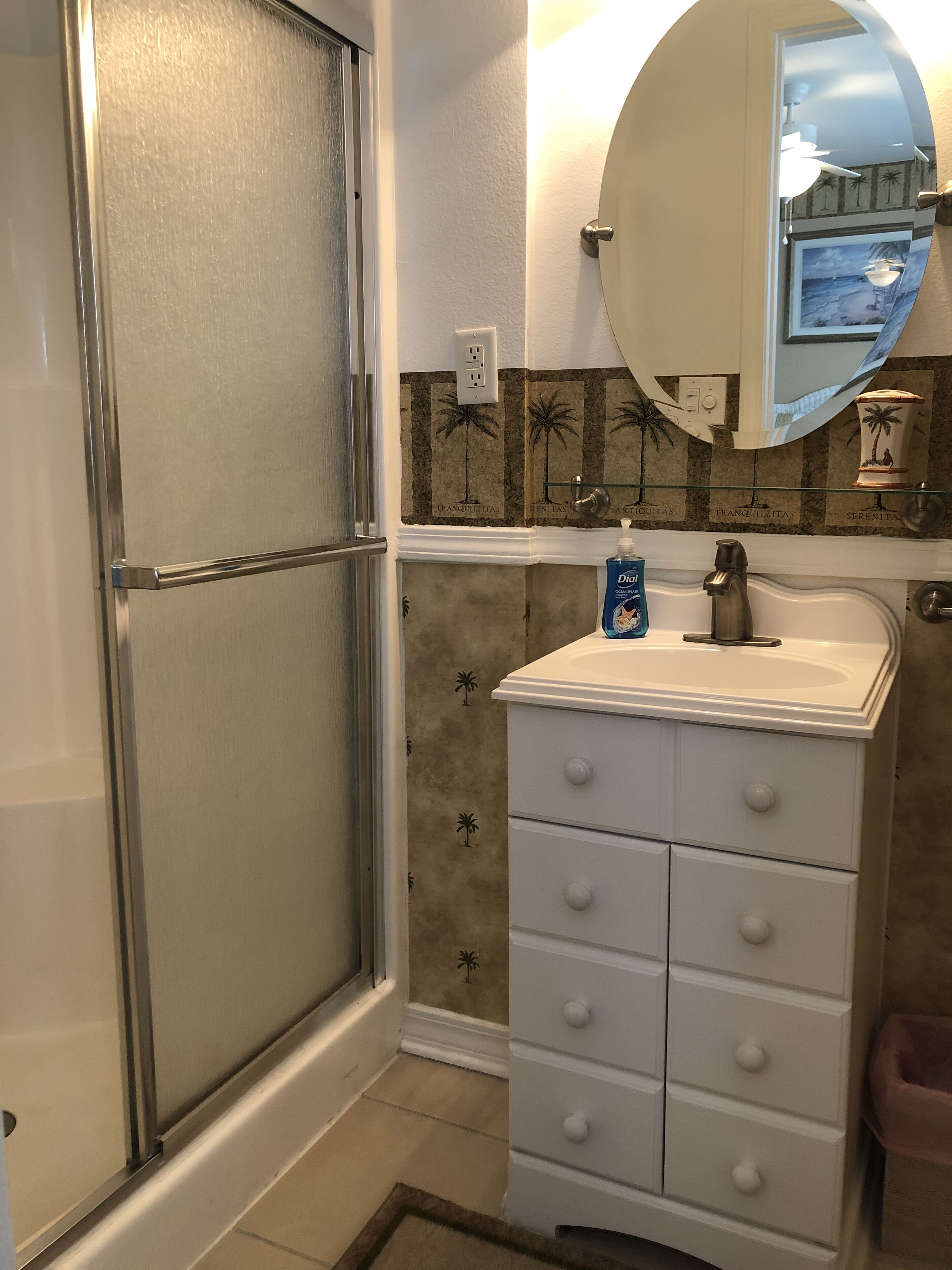 Une salle de bain avec une douche, un lavabo avec un miroir au-dessus et un porte-serviettes.