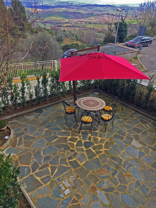 A patio with stone flooring, a round table, and four chairs with yellow cushions.