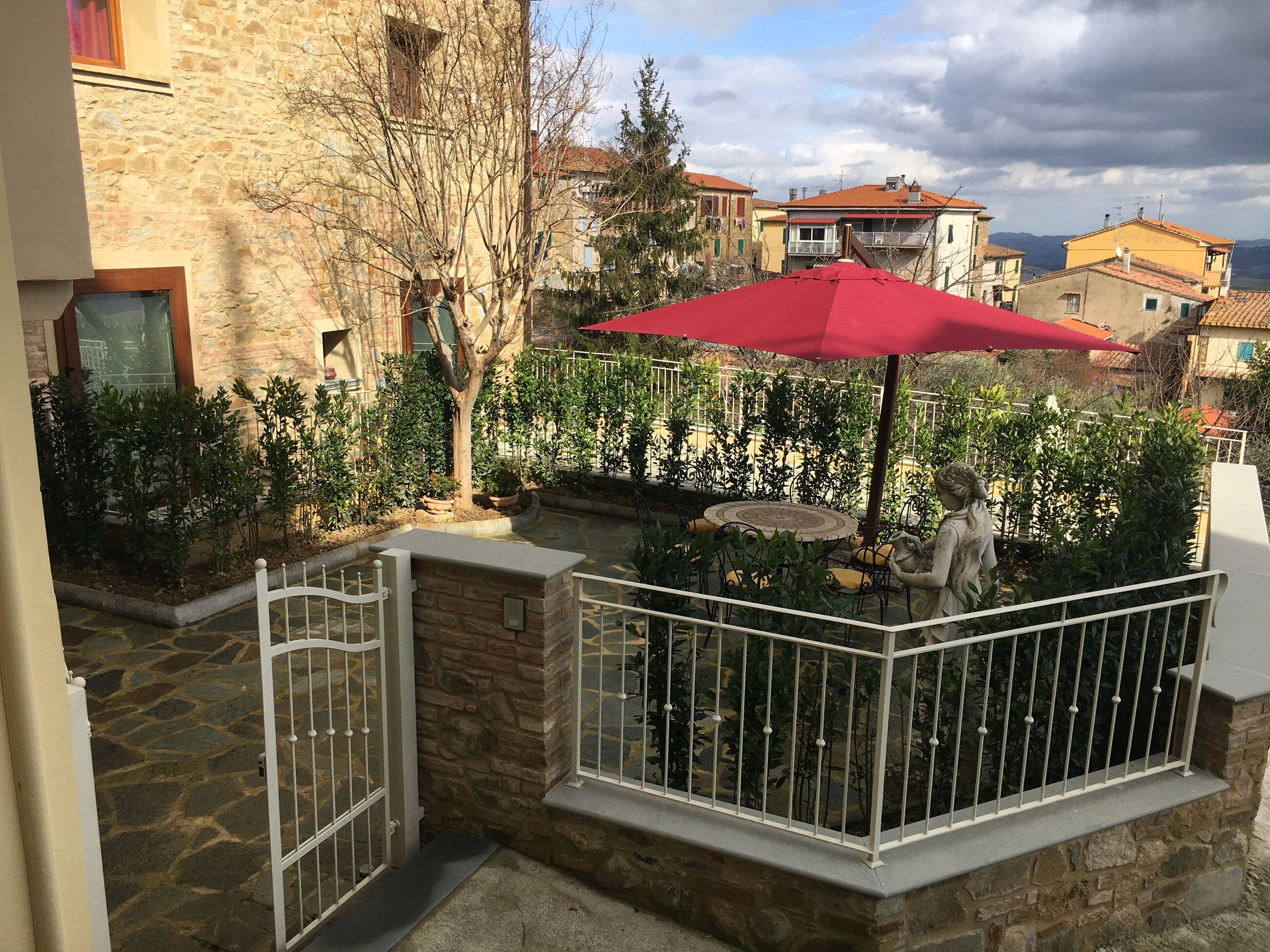 A stone courtyard with a red umbrella, a statue, and a stone wall.