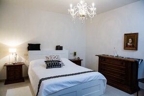 Un dormitorio con una cama, un tocador, una mesita de noche, una araña y un cuadro enmarcado en la pared.