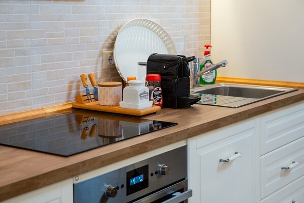 A kitchen with a modern design, featuring a black induction cooktop, a coffee maker, a kettle, and a coffee grinder on the counter.