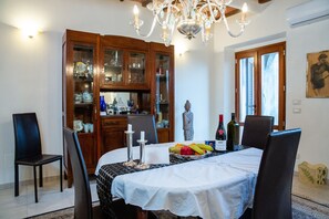 Un comedor con una mesa dispuesta para cuatro personas, rodeado de armarios de madera con puertas de cristal, una araña y una estatua en la pared.
