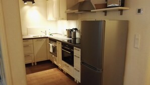 A compact kitchen with a built-in oven, a stainless steel refrigerator, and a microwave on a shelf. - the old. house - Apartment "The Oben" (Göttingen)