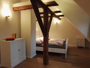Ein Schlafzimmer mit schrägem Dach, Holzbalken, einem Bett mit Kissen, einem Nachttisch und einem Kleiderschrank.