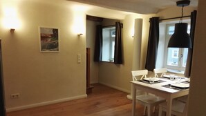 A dining area with a white table and chairs, a painting on the wall, and a window with curtains. - the old. house - Apartment "The Oben" (Göttingen)