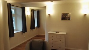 A room with a chair, a white dresser, and two windows with curtains. - the old. house - Apartment "The Oben" (Göttingen)