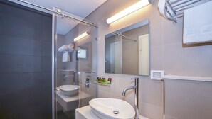 Een moderne badkamer met een glazen douchecabine, een wit wastafeltje en een spiegel erboven.