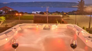 Een jacuzzi met twee glazen rode wijn, met uitzicht op zee en een golfbaan.
