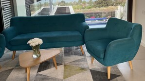 Een moderne woonkamer met een blauwgroene bank, twee bijpassende fauteuils, een salontafel en uitzicht op een meer en bergen.