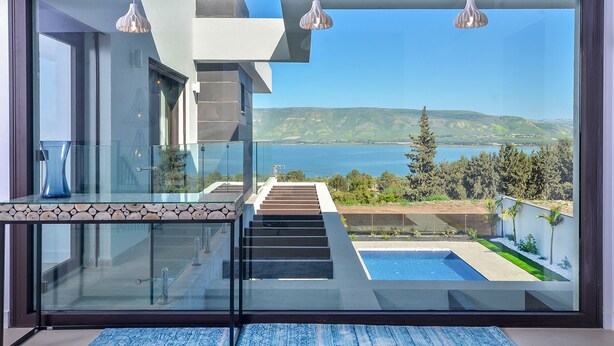 Een modern balkon met glazen hekwerk, een zwembad en uitzicht op zee en heuvels.