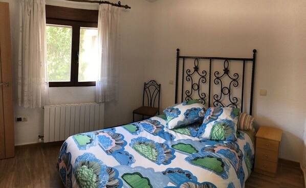 Un dormitorio con cama, mesita de noche, silla, ventana con cortinas y radiador.