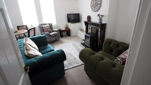 A living room with a sofa, a television, a fireplace, and a clock on the wall. - Lymm village apartment (Lymm)