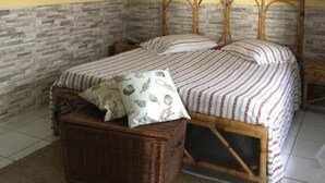 A bedroom with a bed, a wicker basket, a wall-mounted circular decoration, and a textured wall. - Pousada Nel Blu (Itaparica)