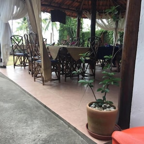 An outdoor dining area with tables and chairs, surrounded by potted plants and a covered structure. - Pousada Nel Blu (Itaparica)