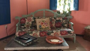 A room with a floral sofa, a table with a bowl and remote controls, and a blue door. - Pousada Nel Blu (Itaparica)