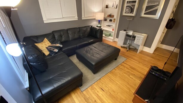 A modern living room with a black leather sofa, a wooden floor, and a grey wall. - Beaumont Nurses or Dr’s need quarantine site?<br>Downtown Royal Oak, charming 2bd (Royal oak)