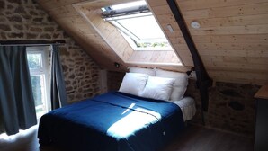 Een slaapkamer met een schuine plafond, een dakraam, een bed met witte kussens en een blauwe dekbedovertrek.