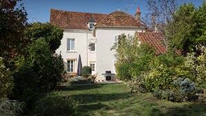Ein zweistöckiges Haus mit rotem Ziegeldach, einer kleinen angebauten Garage und einem gepflegten Garten mit verschiedenen Pflanzen und Sträuchern.