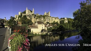 Eine historische Burg auf einem Hügel mit Blick auf eine Stadt, im Vordergrund fließt ein Fluss.