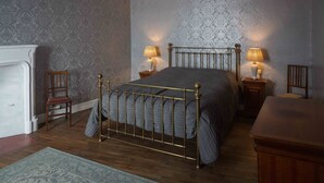 Ein Schlafzimmer mit einem Bett, zwei Nachttischen, einem Sessel, einer Kommode und einem Kamin.