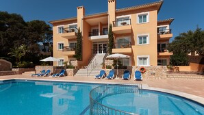 Un hotel a più piani con piscina, lettini e una scala che conduce all'ingresso.