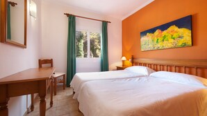 Una camera d'albergo con due letti, una scrivania in legno, una sedia, una finestra con tende, un quadro appeso al muro e una lampada sul comodino.