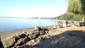 A rocky shoreline with a calm body of water, a wooden structure with a roof, and a large tree on the right. - 40 Acres Estate, Beach Access, Pet Friendly: Wildwood Studio (Vashon)
