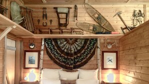 A rustic wooden room with a bed, framed pictures, and various tools hanging on the wall. - 40 Acres Estate, Beach Access, Pet Friendly: Wildwood Studio (Vashon)